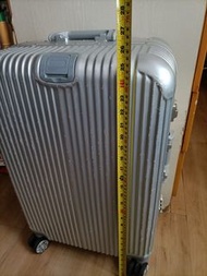 銀色鋁合金行李箱，帶有密碼鎖和可伸縮拉桿。內部有藍色襯裡和固定帶。箱體外觀有條紋設計，底部有四個輪子，方便移動。呎吋：16”x10”xH26”40cmx26cmxH66cm。箱體表面有輕微使用痕跡。運