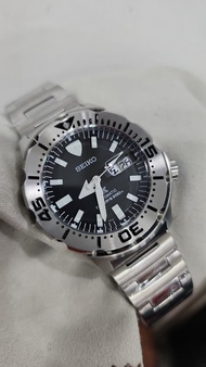 Jam tangan Seiko Monster dengan tali logam dial hitam angka putih dan tanggal.