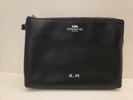 一款印有「A.M」客製化字母的黑色皮革 Coach 零錢包手拿包，帶有經典的金屬 Logo 標誌。