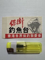 香港民間保釣運動的歷史紀念物品，包含印有「保衛釣魚台」及「香港各界保釣聯委會」字樣與抗議拳頭圖案的貼紙或標語，以及一個黃色的透明打火機。保釣組織：標語上標示「香港各界保釣聯委會」（全稱為香港各界保衛釣