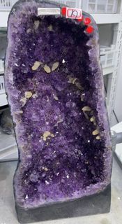 天然紫晶洞，這是一個美麗獨特的鮮艷紫🦄🦄🔮🦄🦄的天然紫晶洞，呈現深紫色，內部充滿閃亮的晶體。洞內還點綴著一些黃色的放假石像一朵花軟體一幅🤩美麗的山水畫🏞️，紫晶洞被放置在一個啡色的底座上，整體外觀完整